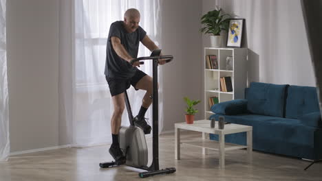 Perder-Peso-Y-Entrenar-El-Sistema-Cardiovascular-Usando-Una-Bicicleta-Estática-En-Casa-Un-Hombre-Adulto-Está-Haciendo-Ejercicios-Deportivos-En-Una-Bicicleta-Estática-En-La-Sala-De-Estar